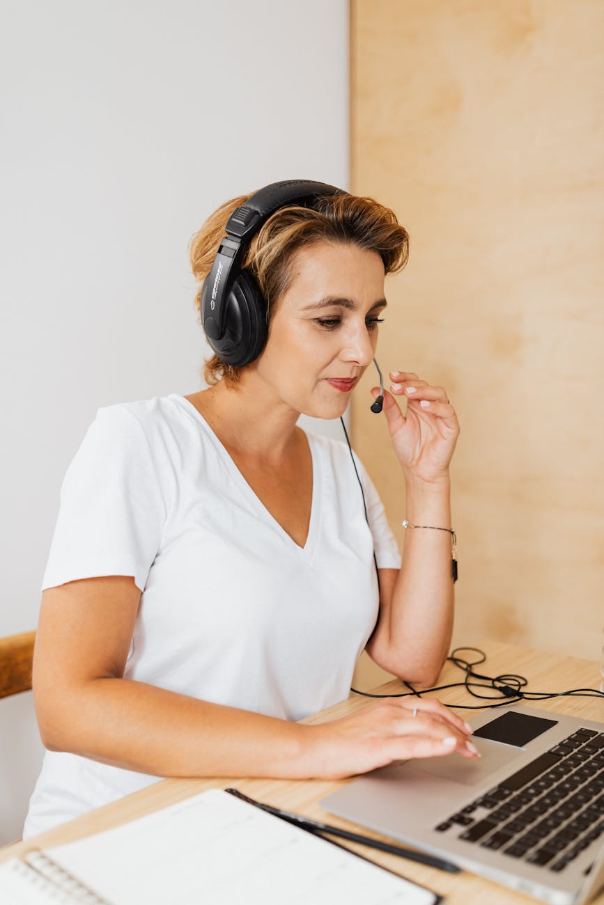 woman in white v neck t shirt wearing a headset while in front of the laptop